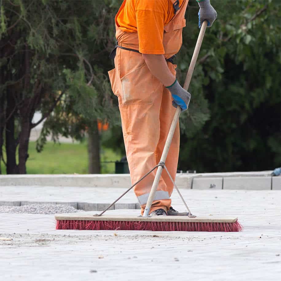 Mann in orangener Arbeitsbekleidung fegt auf einer Baustelle den Weg frei. - Leistungen - BAGER Gebäudereinigung