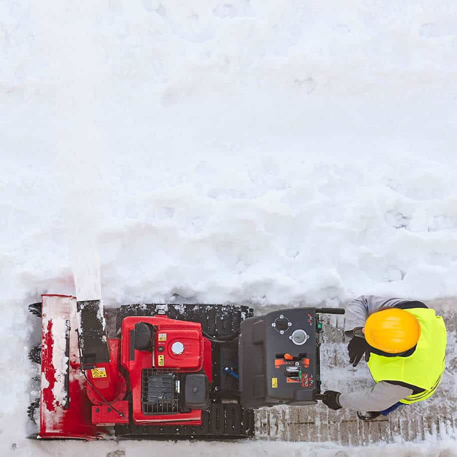 Mann fährt mit Schneefräse über mit Schnee bedecktem Gehweg. - Leistungen - BAGER Gebäudereinigung